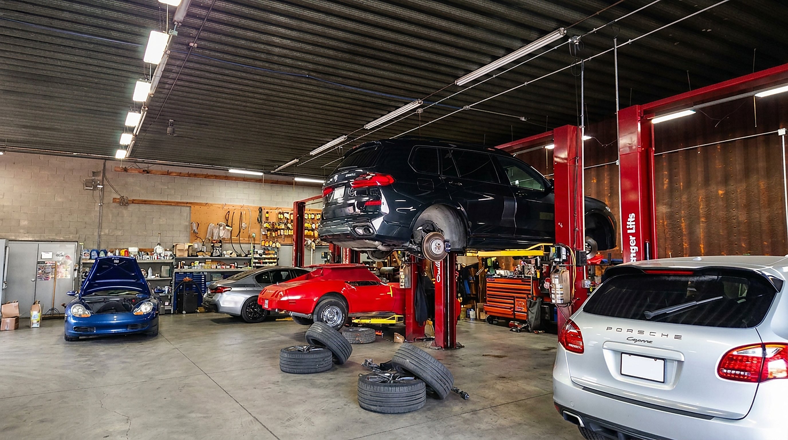 BMW X5 on a lift beside a Porsche Boxster and Corvette in the Madison Motorsports shop